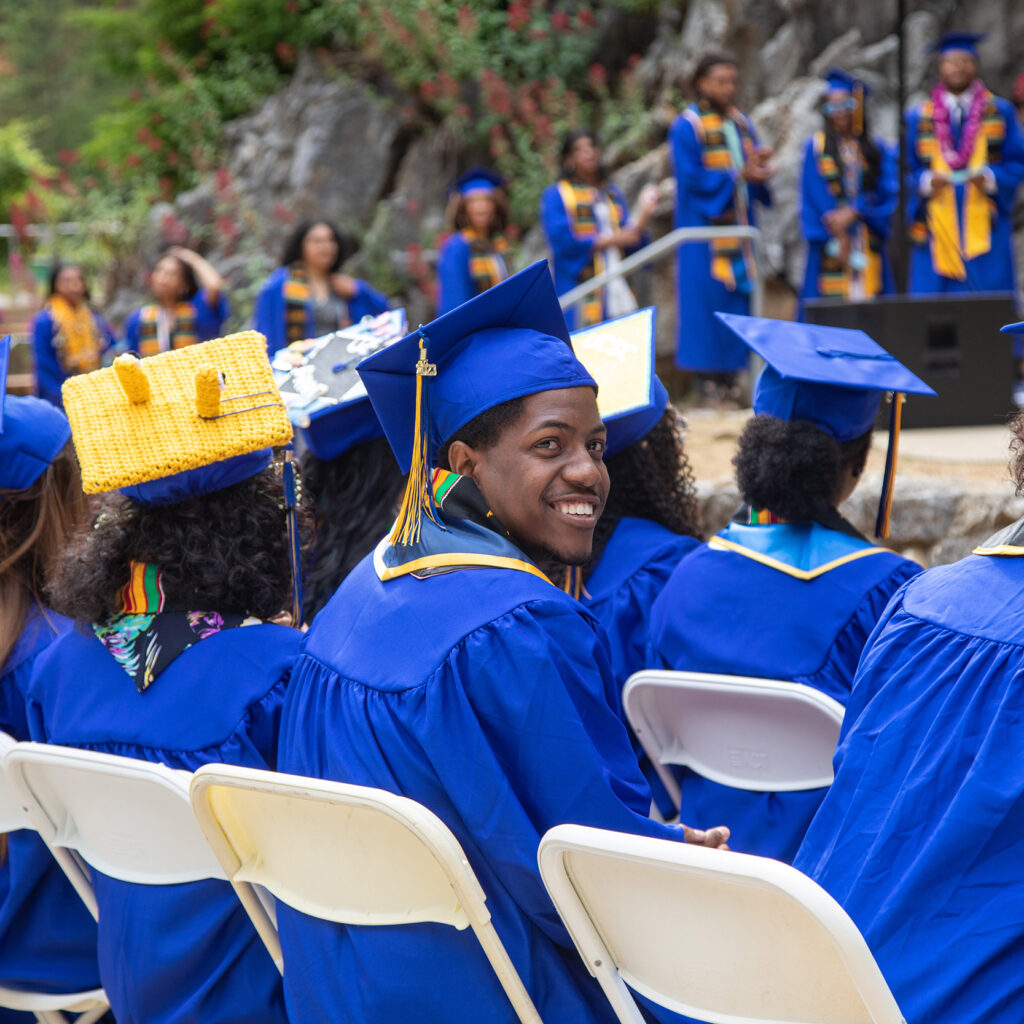 Student seated a tcommencement ceremony smiling and looking at the camera. 