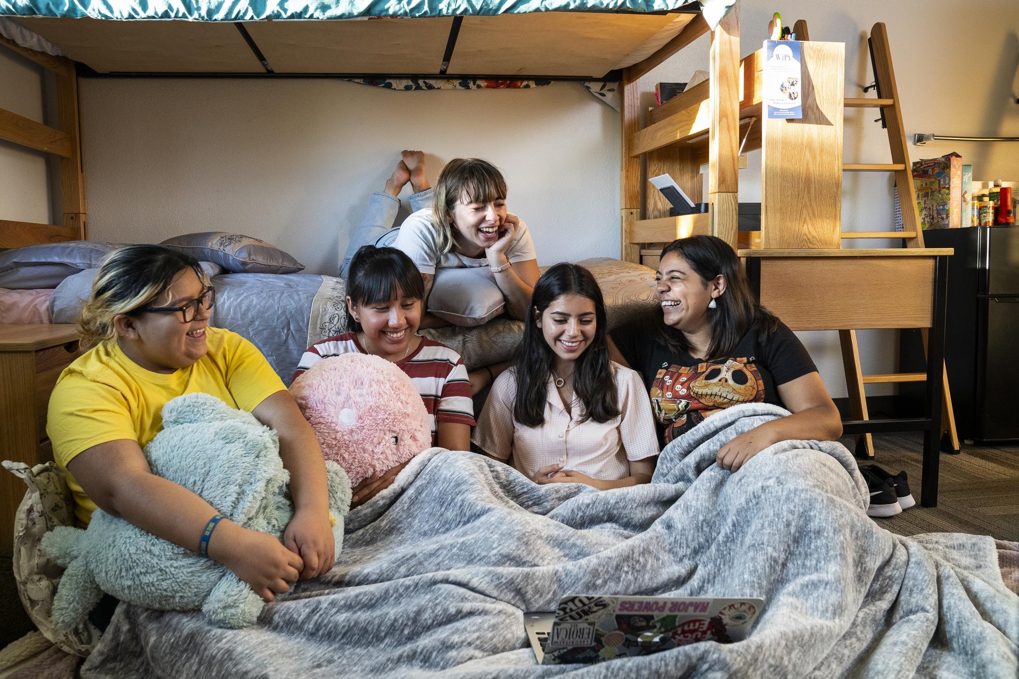 People in a dorm hanging out watching a video on a laptop.